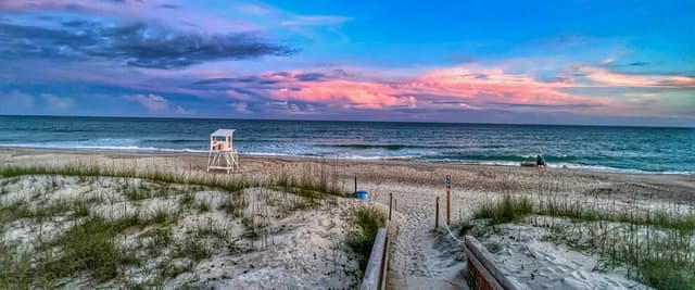 Sunset over Bogue Sound, North Carolina, with pink and purple clouds reflected on calm water and beach grass in the foreground